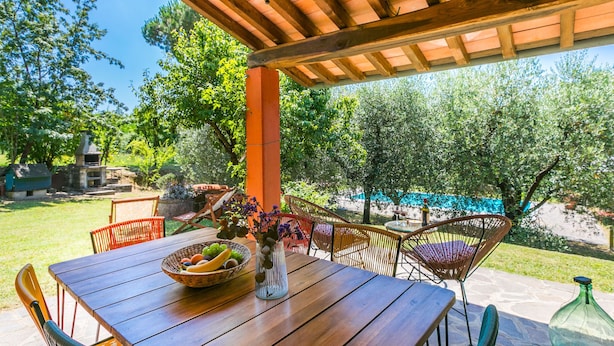 An outdoor patio with a wooden table and chairs, a bowl of fruit, and a vase of flowers. - Podere Cerbaia (SMR100) by Interhome (Santa Maria al Monte)