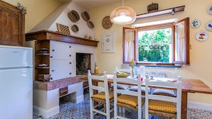 A kitchen with a white refrigerator, wooden cabinets, a built-in oven, and a dining area with a table and chairs. - Podere Cerbaia (SMR100) by Interhome (Santa Maria al Monte)