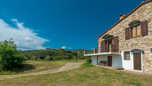 Una casa de piedra con un balcón, una banca de madera y una vista despejada del paisaje circundante.