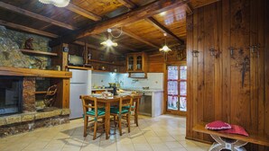 A rustic kitchen with wooden beams, a stone wall, a dining table with chairs, and a bench.