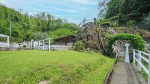 A rustic cabin with a stone foundation, surrounded by lush greenery and a stone pathway leading to it.
