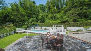 An outdoor patio with stone flooring, a pool, and a dining area with chairs and tables.