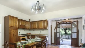 A kitchen with wooden cabinets, a dining table set with plates and glasses, a chandelier, and a view through an open doorway to an outdoor area. - La Mangiatoia (TER104) by Interhome (Terricciola)