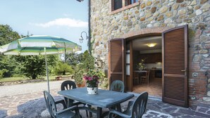 Un edificio de piedra con un patio que incluye una mesa y sillas, una puerta abierta que da al interior y un paraguas verde.