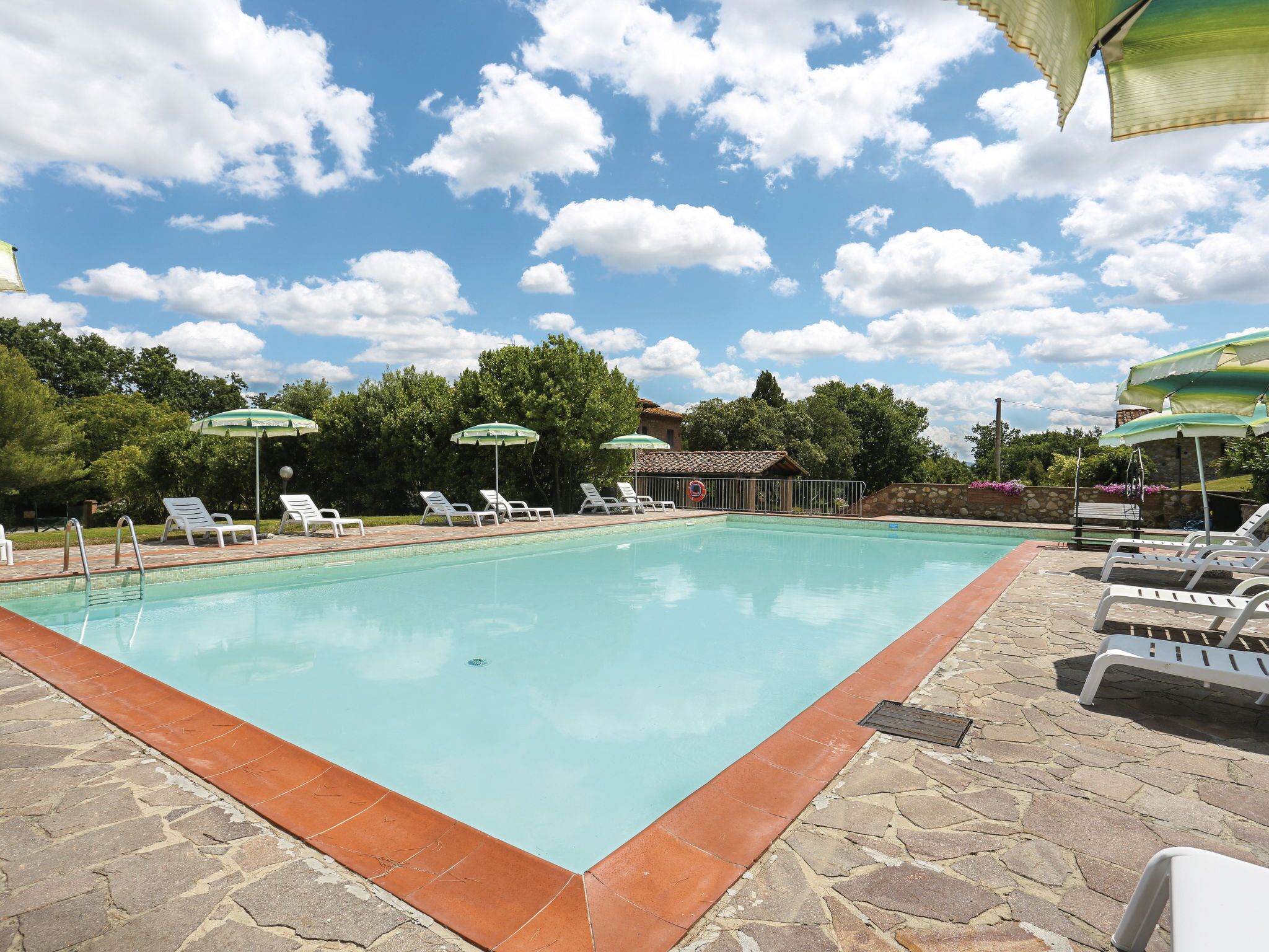A swimming pool with lounge chairs and umbrellas, surrounded by stone tiles and greenery.