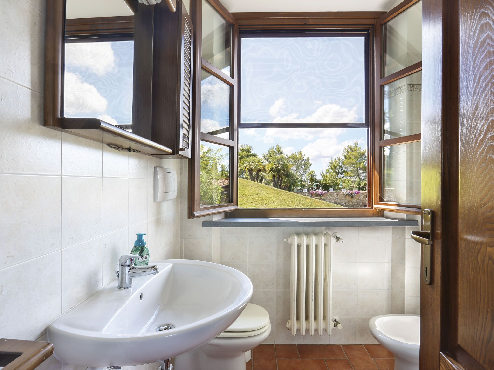 A bathroom with a large window, a sink, a toilet, and a radiator.