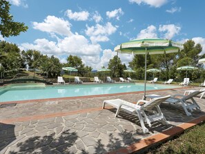 A swimming pool with white lounge chairs and green umbrellas, surrounded by stone tiles and greenery.