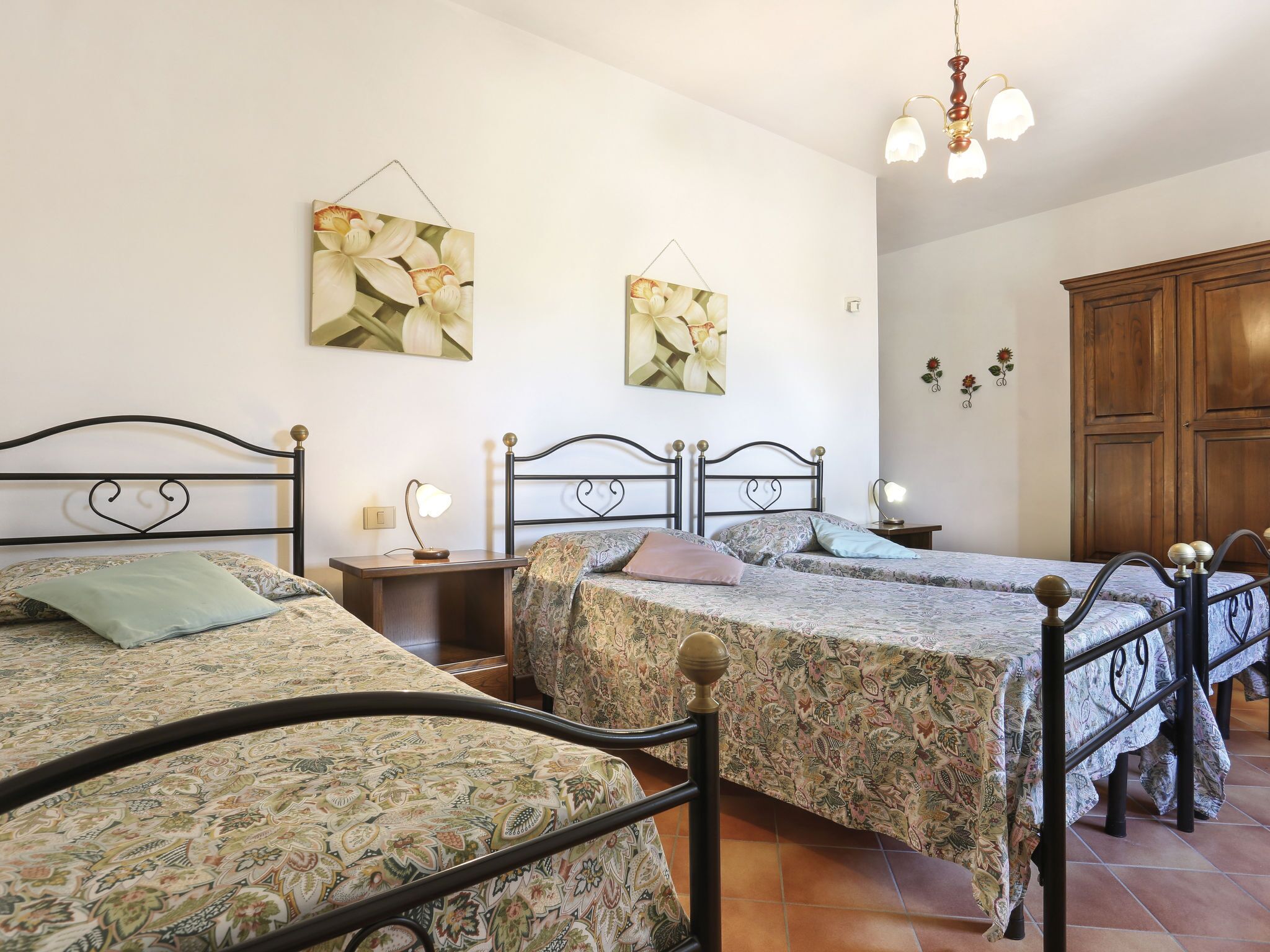 A bedroom with two beds, a wooden wardrobe, and floral artwork on the walls.
