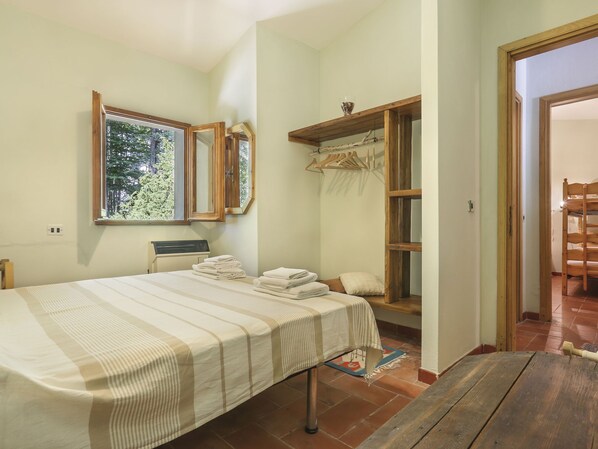 Un dormitorio con cama, ventana, espejo, estante con ropa y una mesa de madera.