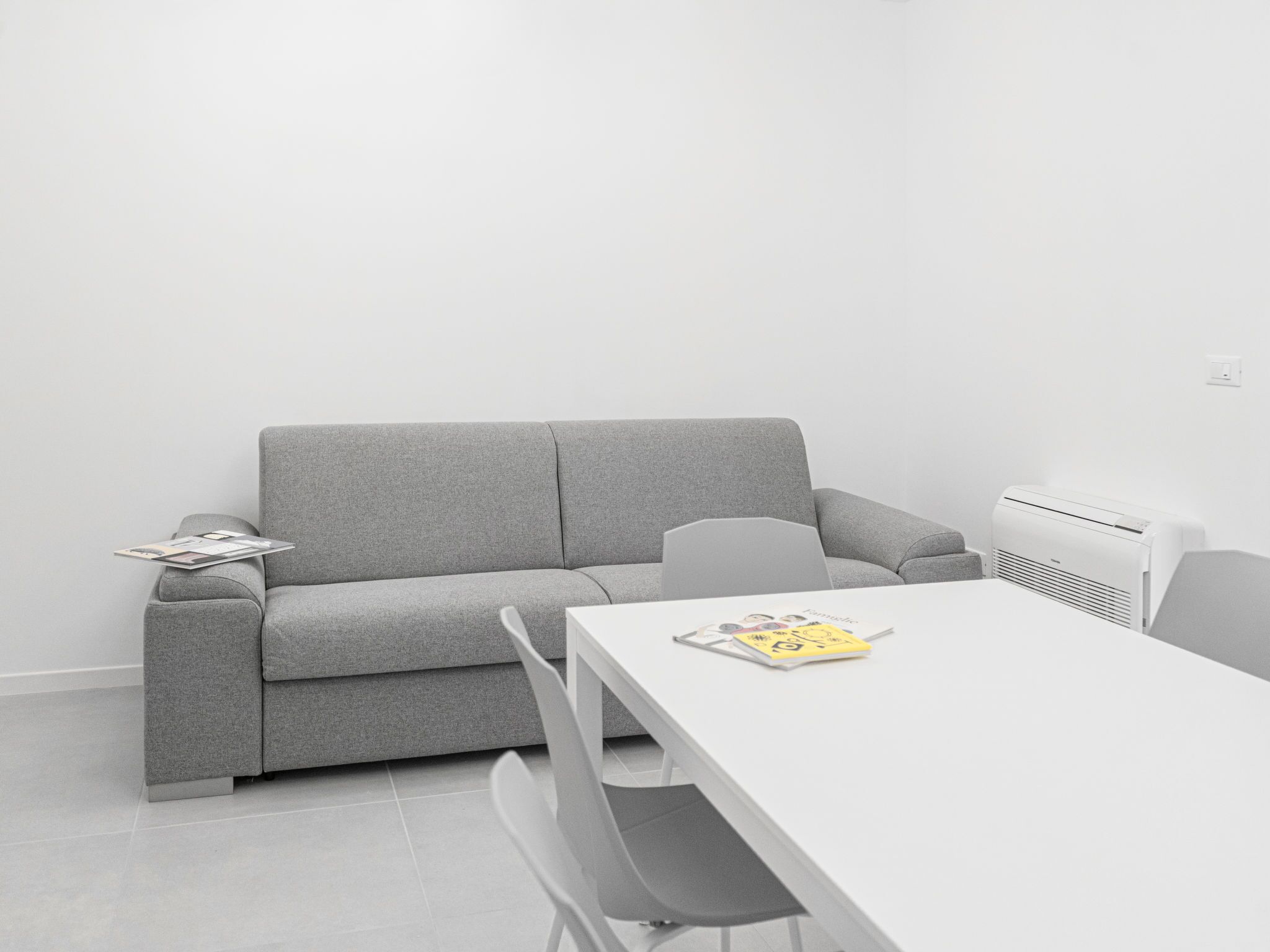 Ein modernes, minimalistisches Zimmer mit einem grauen Sofa, einem weißen Tisch und einer weißen Klimaanlage.