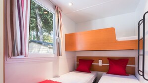 A compact room with two single beds, each with a red pillow and white bedding. A window with curtains is visible, and a bunk bed is positioned above the beds. - Camping Village Mare Pineta by Interhome (Sistiana-Duino-Aurisina)