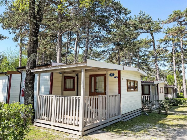 A row of mobile homes with a wooden porch, surrounded by tall trees.