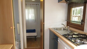 Eine kleine Küche mit Herd, Spüle und einem Fenster mit Jalousien.