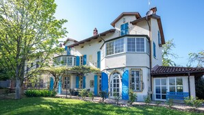Une maison à deux étages avec un balcon, un petit jardin et un banc bleu.