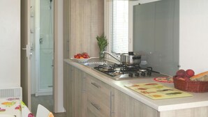 Una cucina moderna con piano cottura a gas, lavello e pensili in legno. Si vede una finestra con persiane, una pianta e un cesto di frutta sul piano di lavoro.