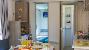 Una camera d'albergo compatta con angolo cottura, zona pranzo con tavolo apparecchiato per due e letto con copripiumino blu.