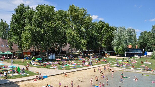 Una spiaggia con persone che prendono il sole, nuotano e giocano.
