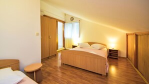 A bedroom with a wooden bed, a bedside table, a nightstand, a wardrobe, and a small stool. - Apartment Peric by Interhome (Korčula/Korčula)