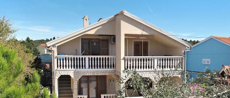 A two-story house with a balcony, a stone entrance, and a small garden area.