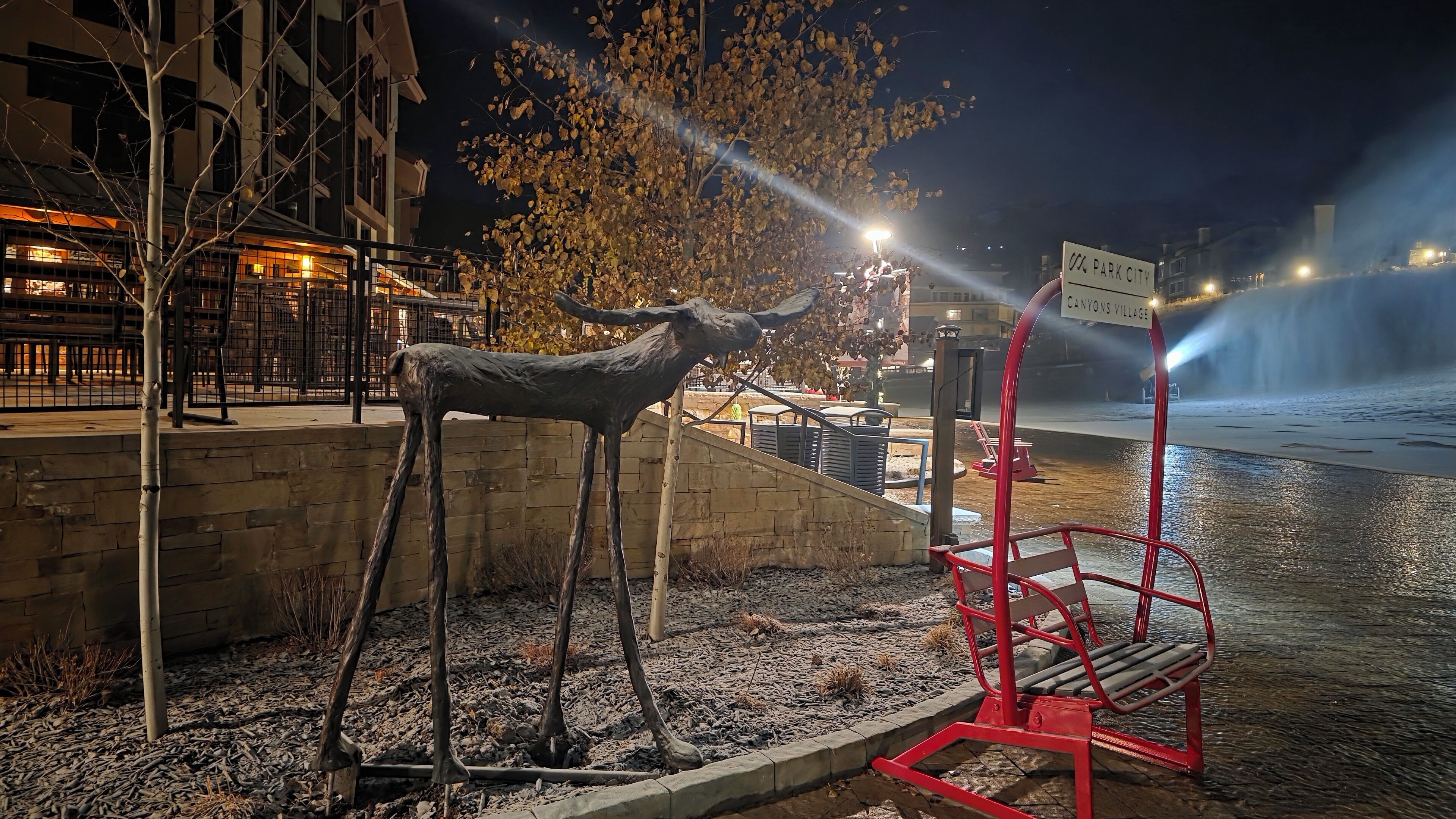 A night scene with a statue of a bull, a red bench, and a sign reading "CANYONS VILLAGE".