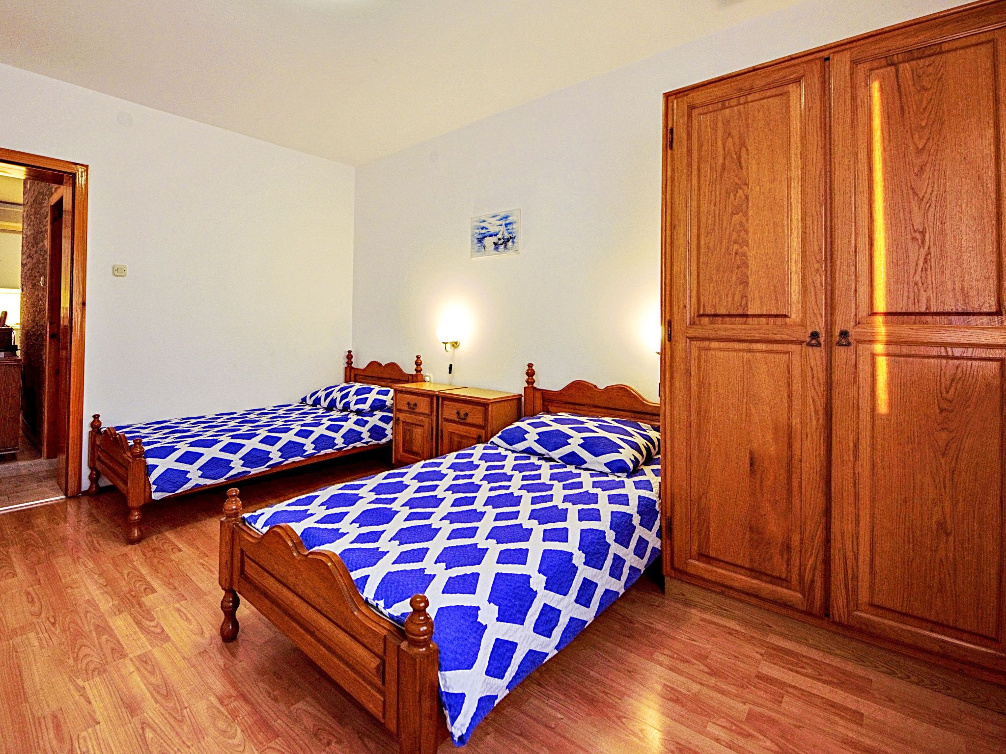 Une chambre à coucher avec deux lits en bois, une armoire en bois et une table de chevet avec une lampe.