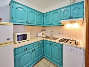 A kitchen with teal cabinets, a white microwave, a coffee maker, a sink, and a dishwasher.