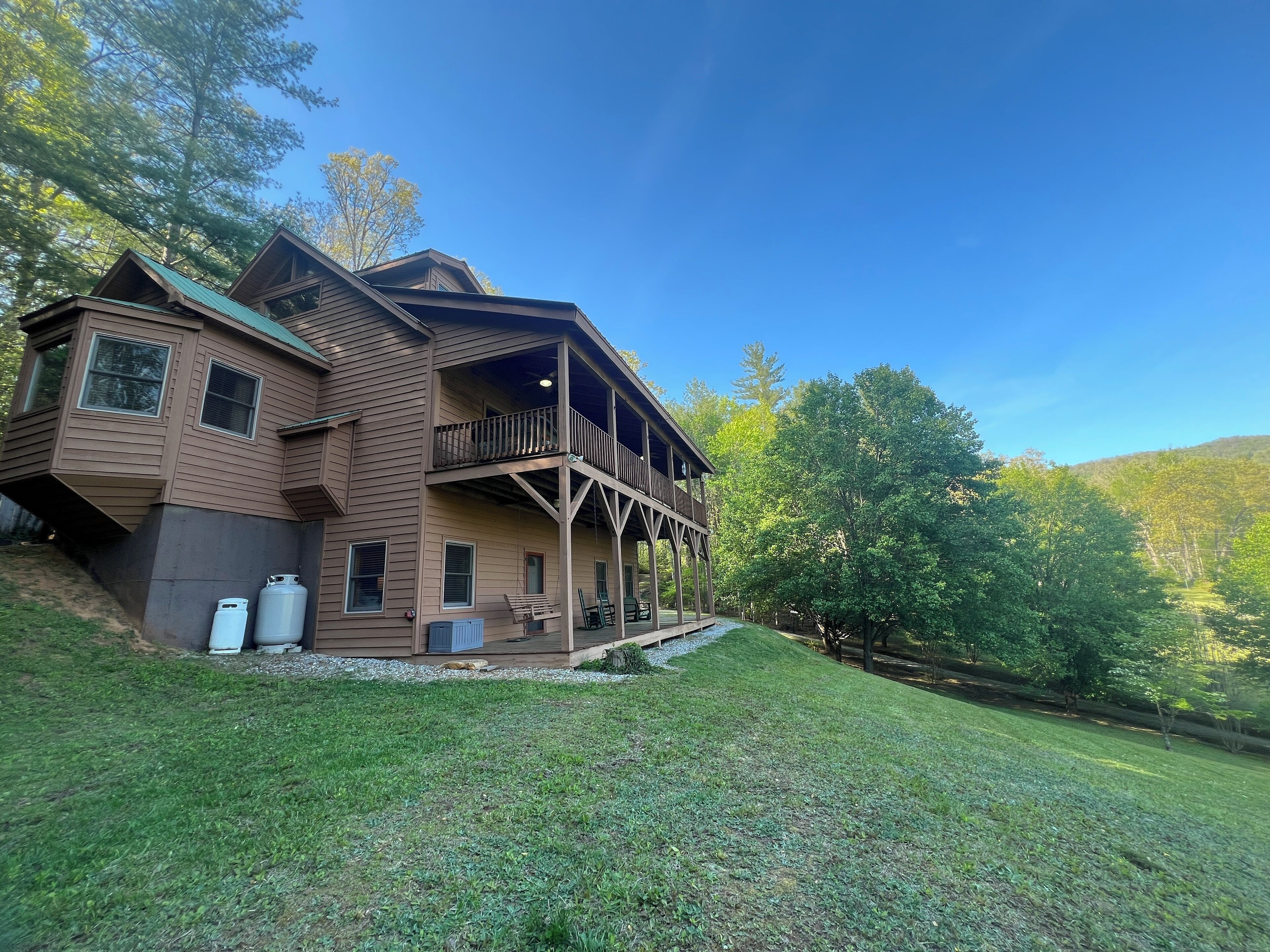 A two-story wooden house with a balcony, a covered porch, and a grassy yard.