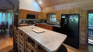 A cabin-style kitchen with wooden cabinets, a granite countertop, a black refrigerator, and a dining area with wooden chairs.