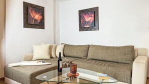 Una sala de estar con un sofá, una mesa de centro de vidrio, una botella de vino y dos cuadros con motivos florales en la pared.