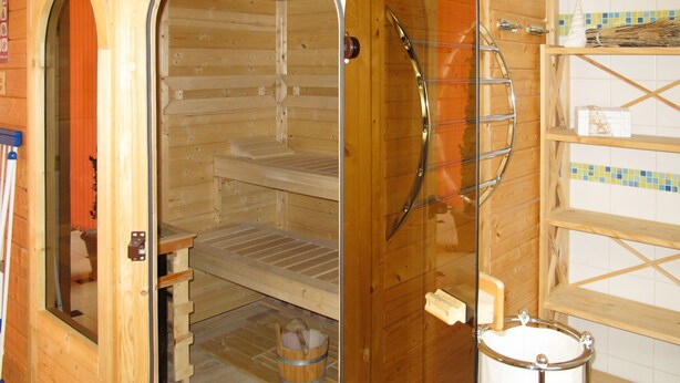 A sauna with wooden walls and a bench. There is a small table and a bucket on the floor.