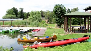 A serene lakeside setting with several kayaks and canoes docked at the edge of the water, a grassy area, and a wooden pavilion. - Zum Stolpseefischer by Interhome (Himmelpfort)