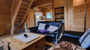 A wooden cabin interior with a staircase, a black leather sofa, a wooden chest, and a kitchen area in the background. - Zum Stolpseefischer by Interhome (Himmelpfort)