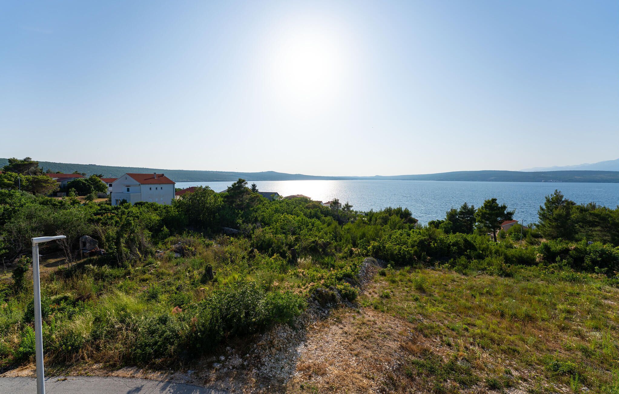Paisatge costaner amb una vista clara del mar, un edifici blanc amb teulada vermella i un camí que condueix cap a l'aigua.