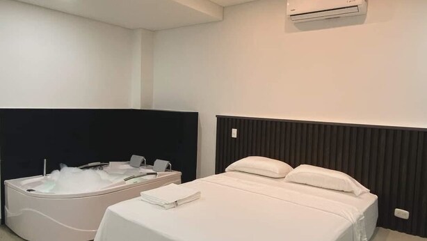 Una habitación de hotel moderna con una cama grande, una bañera independiente y un equipo de aire acondicionado instalado en la pared.
