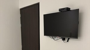 Una habitación con una puerta de madera oscura, un televisor de pantalla plana montado en la pared y una lámpara en el techo.