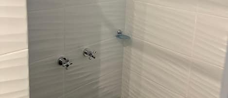 A shower with a handheld showerhead and a glass soap dish.