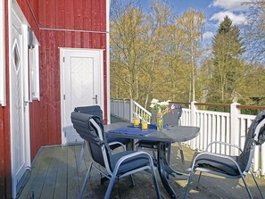 Un bâtiment rouge avec une porte blanche, une table en verre entourée de chaises et une clôture blanche.