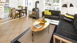 A modern living room with a wooden staircase, a sofa, a dining table with chairs, and a wood-burning stove. - Falster by Interhome (Bad Saarow)