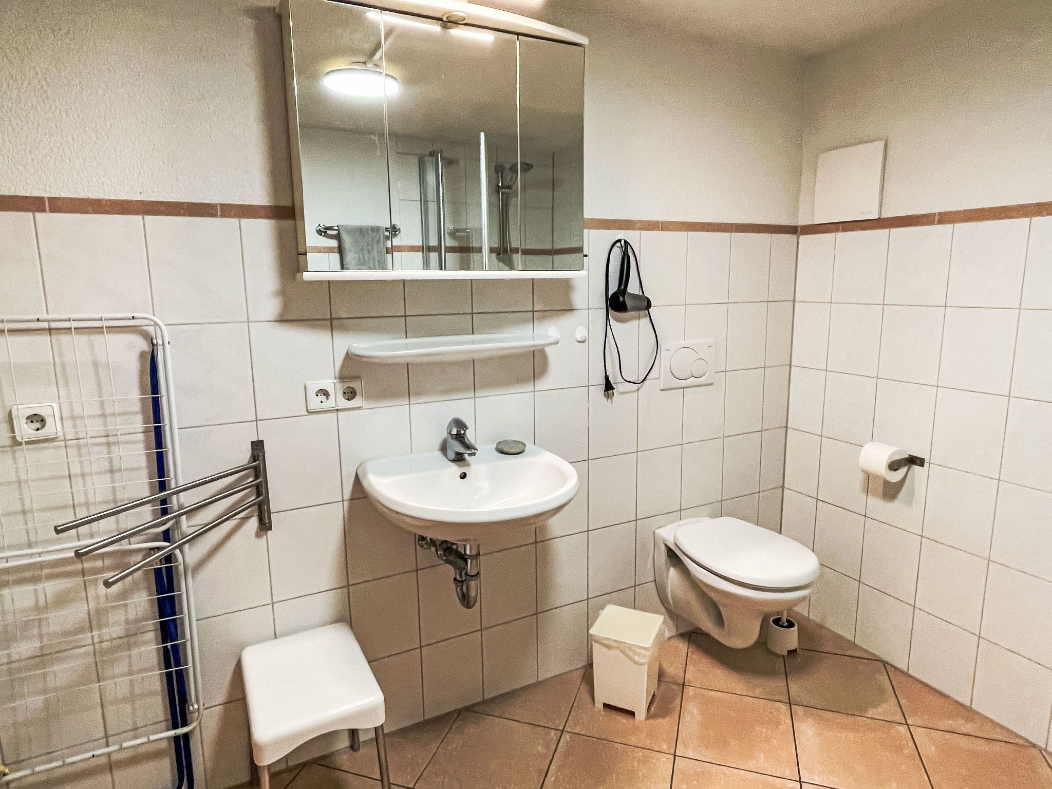 A bathroom with a sink, mirror, toilet, and a small step stool.