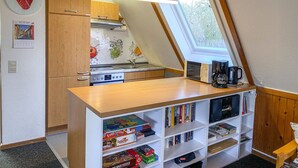Eine kleine Küche mit Fenster, einer Kaffeemaschine und einem Bücherregal voller Bücher.