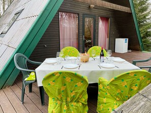 Uma sala de jantar com uma mesa posta para quatro pessoas, cadeiras com estofamento floral, uma pequena mesa com uma vela e uma geladeira ao fundo.