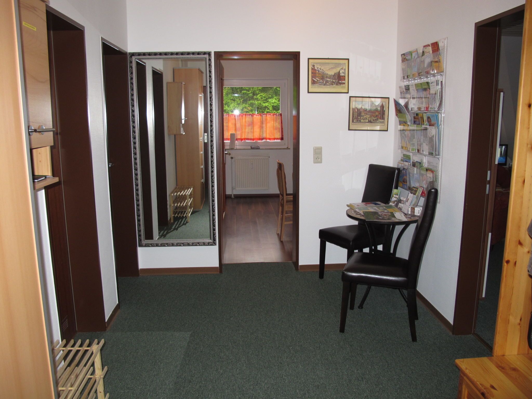 A small room with a wooden door, a mirror, a table with a chair, and a bulletin board with pictures and notes.