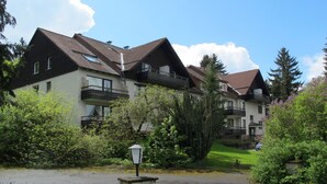 Une rangée d’immeubles modernes à plusieurs étages, dotés de balcons, et entourés d’une végétation luxuriante et d’arbres.