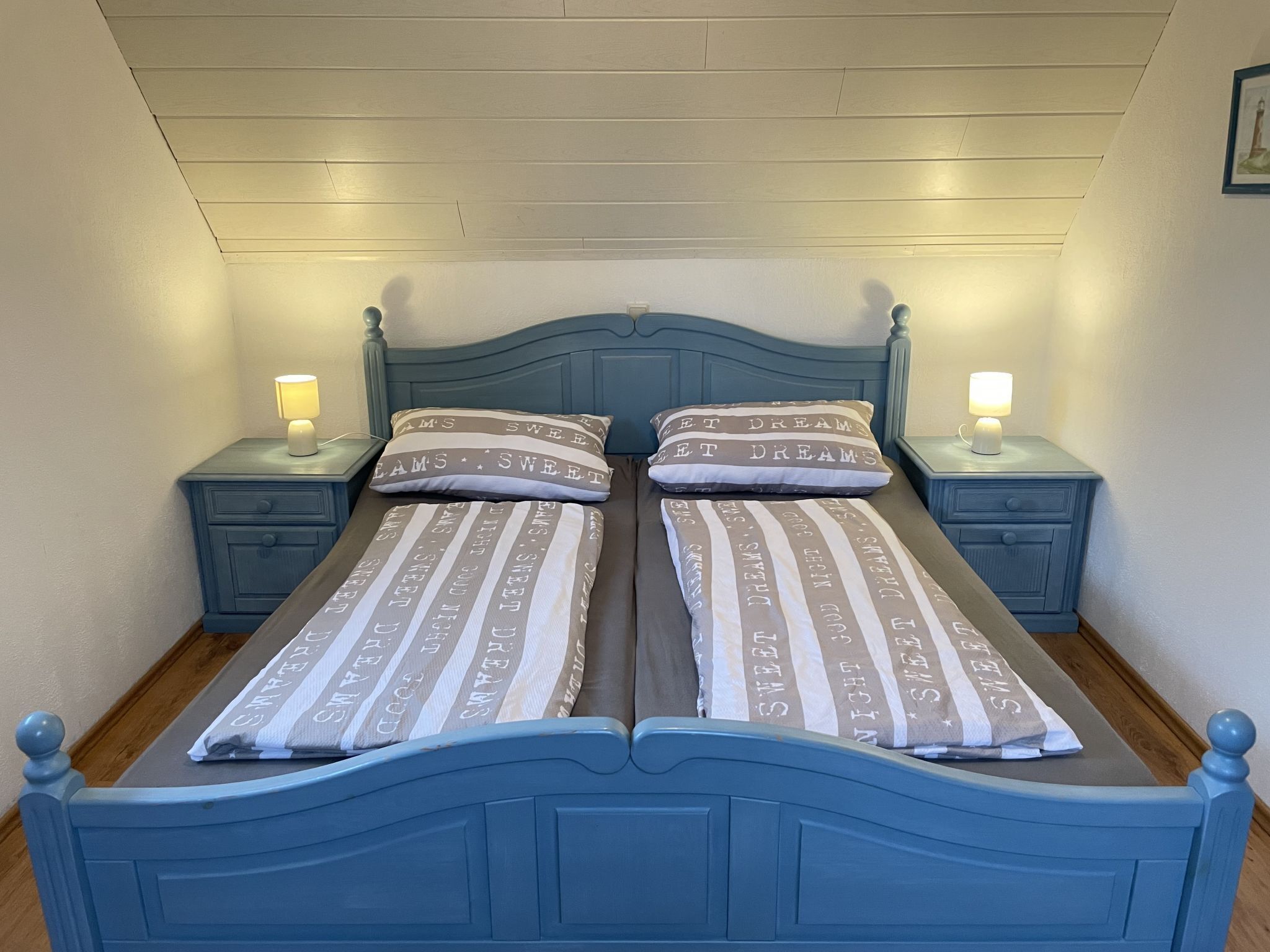 Una cama con dos camas individuales, ropa de cama a rayas y almohadas a juego, dos mesitas de noche con lámparas y un cabecero de madera.