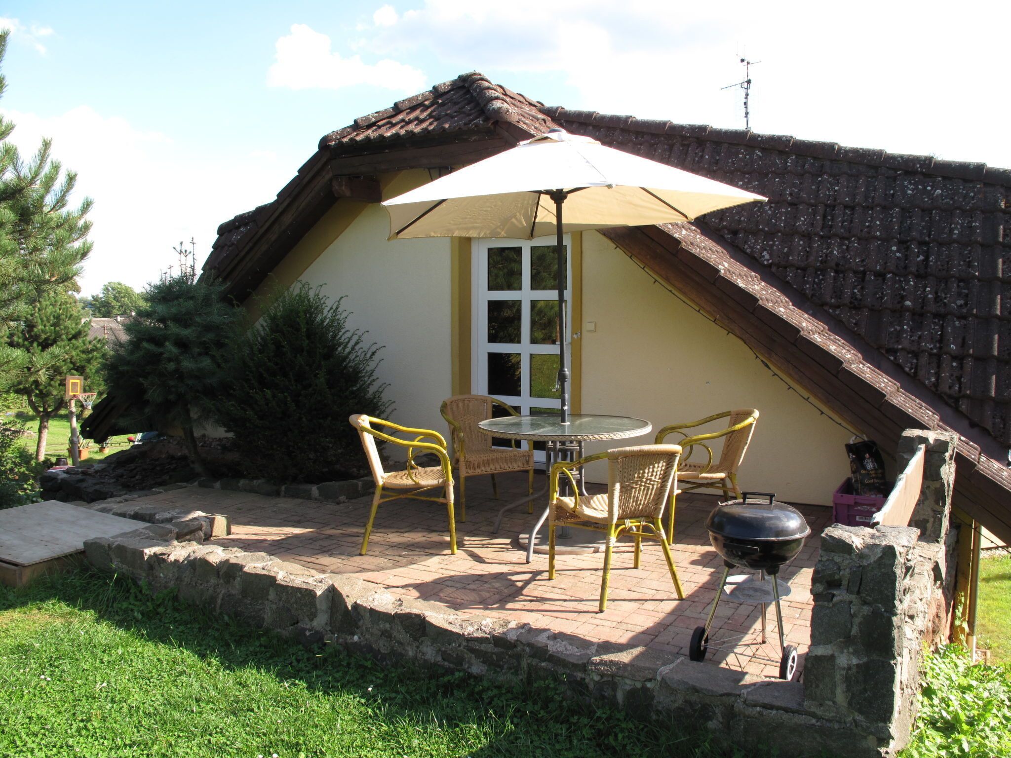 Un patio con mobiliario exterior, una parrilla y un paraguas grande.