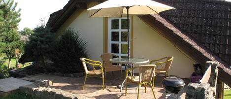 Un patio con mobiliario exterior, una parrilla y un paraguas grande.