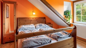 A bedroom with a sloped ceiling, a wooden bed frame, a nightstand, a dresser, and a window with a view of trees.