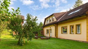 A two-story house with a tiled roof, a small garden, and a wooden bench.
