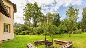 A backyard with a wooden fire pit and picnic tables, surrounded by trees and a house.