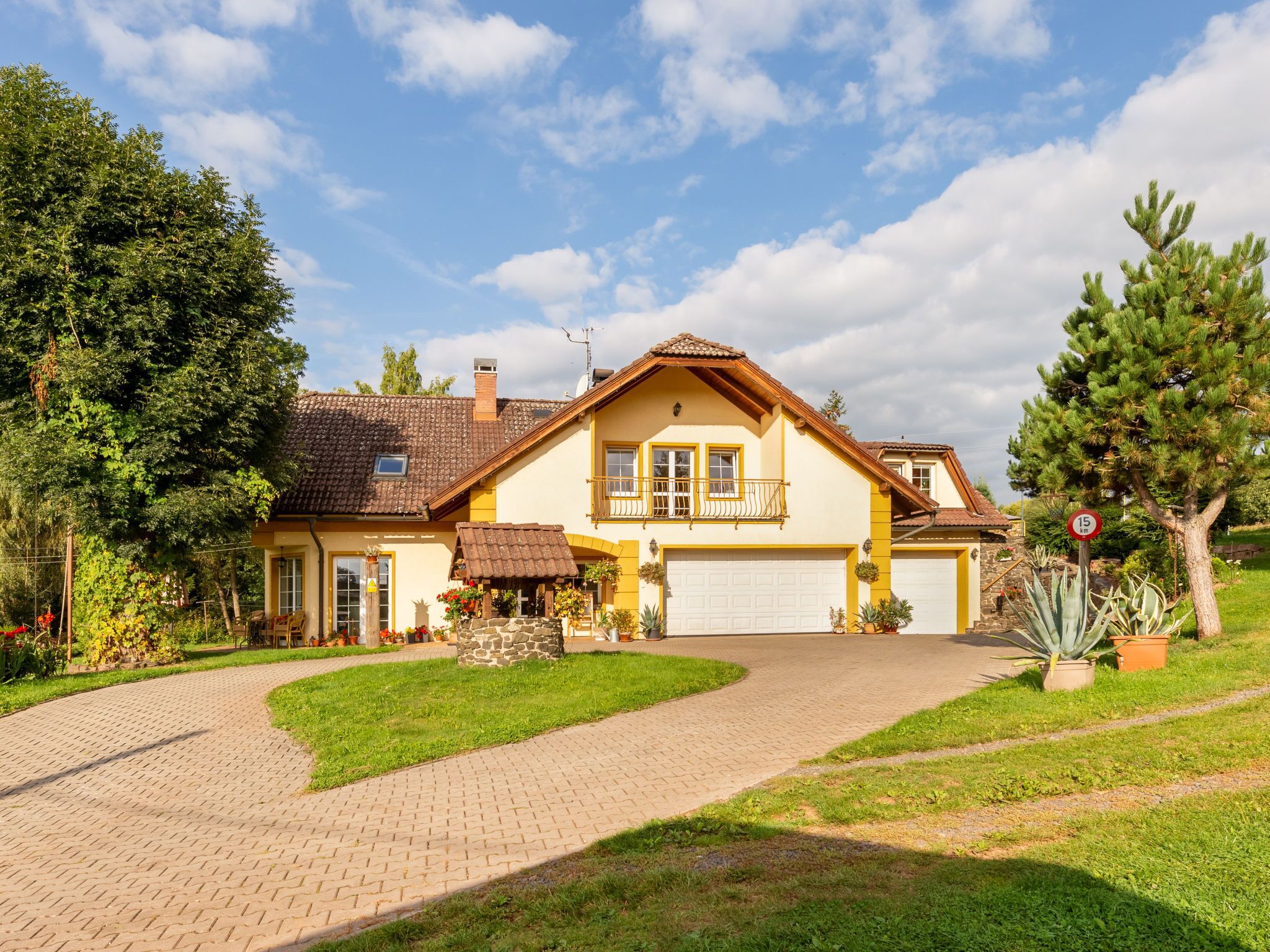 A two-story house with a garage, surrounded by a paved driveway and lush greenery.